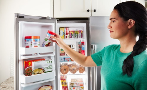 一个女人从法式门冰箱的冷冻室里拿出冷冻水果